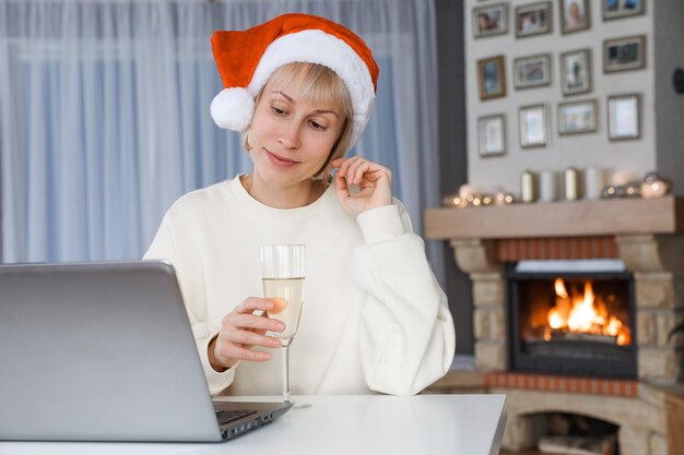 Eine Frau mit Weihnachtsmütze hält ein Glas Champagner Verwandte und Freunde auf einem Laptop zu Weihnachten