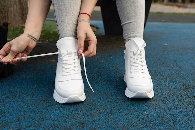 Eine Frau mit weißen Schuhen bindet einen Schnürsenkel.