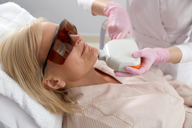 Eine Frau mittleren Alters, die eine Laserbehandlung in einer Kosmetikklinik erhält und eine Schutzbrille trägt