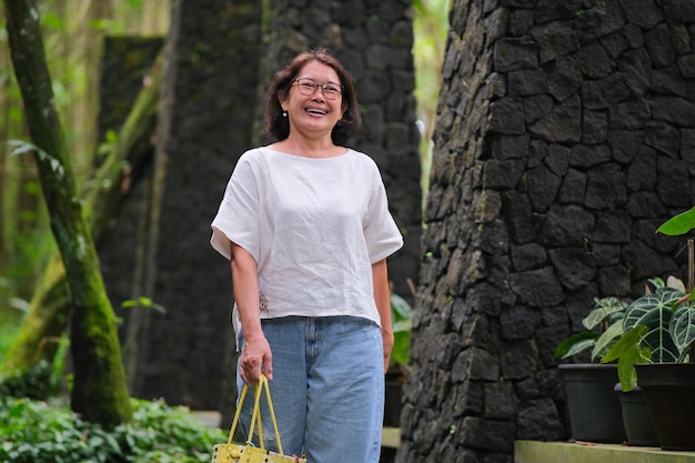 Eine Frau mittleren Alters, die eine Tasche trägt, geht in einem glücklichen Gesicht des Parks spazieren