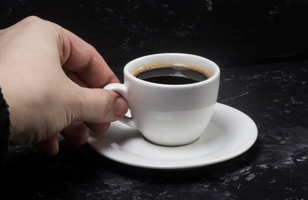 Eine Frau nimmt eine weiße Tasse mit schwarzem aromatischem Kaffee in die Hand, um den Geschmack zu genießen.