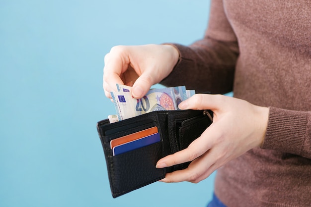 Eine Frau nimmt Geld aus einer Brieftasche auf einem blauen Hintergrund mit einem Platz für Text heraus. Zahlungskonzept.