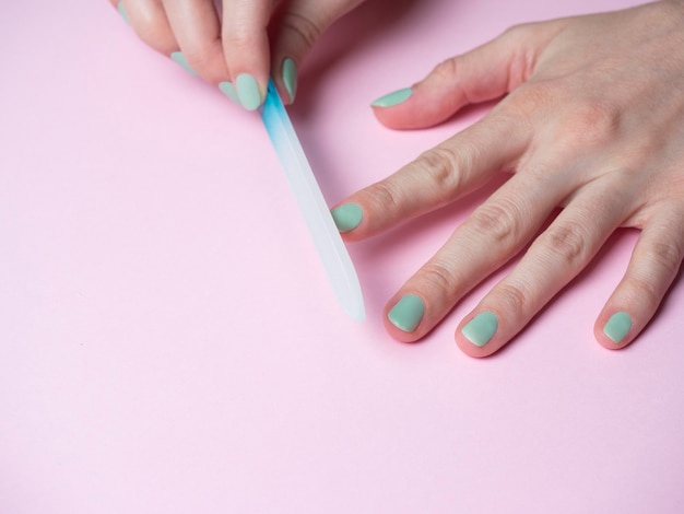 Eine Frau selbst feilt ihre Nägel mit einer Nagelfeile an der Hand auf einem rosa Hintergrund. Handnagelpflege zu Hause. Schönheit und Gesundheit