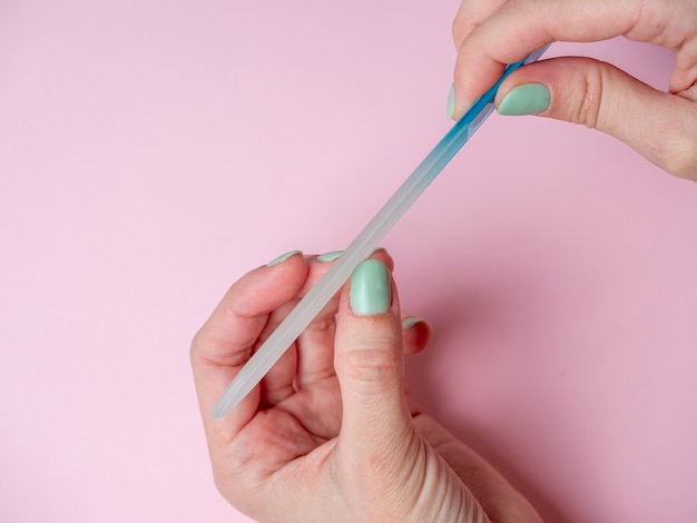 Eine Frau selbst feilt ihre Nägel mit einer Nagelfeile an der Hand auf einem rosa Hintergrund. Handnagelpflege zu Hause. Schönheit und Gesundheit