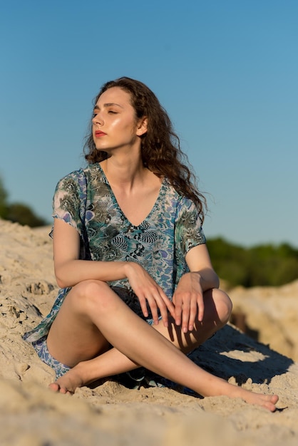 Eine Frau sitzt am Strand und trägt ein blaues Kleid mit Blumenmuster.