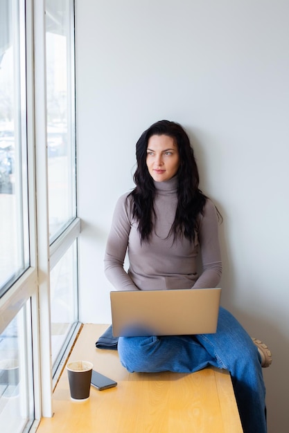 Eine Frau sitzt auf einem Fensterbrett und schaut auf einen Laptop.