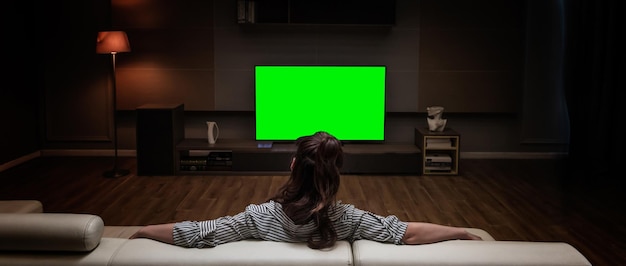 Eine Frau sitzt auf einer Couch vor einem Greenscreen in einem Wohnzimmer.