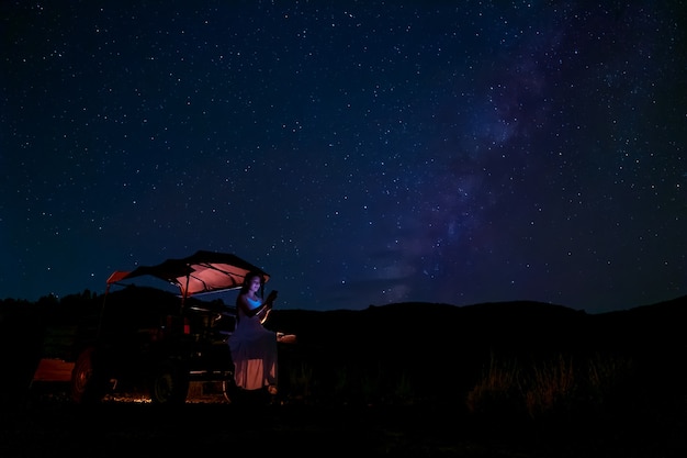 Eine Frau sitzt im Auto eines Bauern und blickt in die Sterne am Nachthimmel, im Hintergrund die Milchstraße.