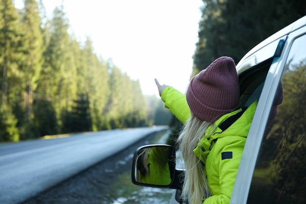 Eine Frau sitzt in einem Auto und zeigt mit dem Finger auf den Fichtenwald