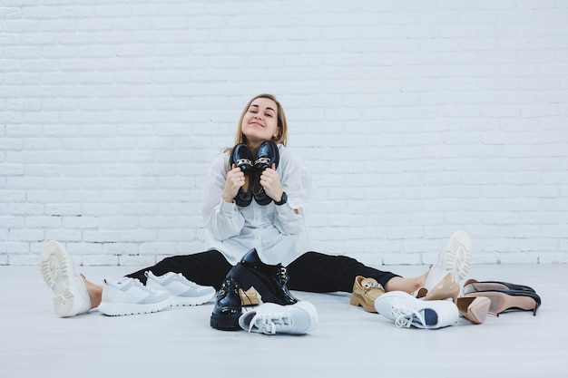 Eine Frau sitzt in einer Umkleidekabine zwischen Schuhen auf dem Boden und sucht sich neue Schuhe aus Dame in weißem Hemd Frau in weißen Schuhen