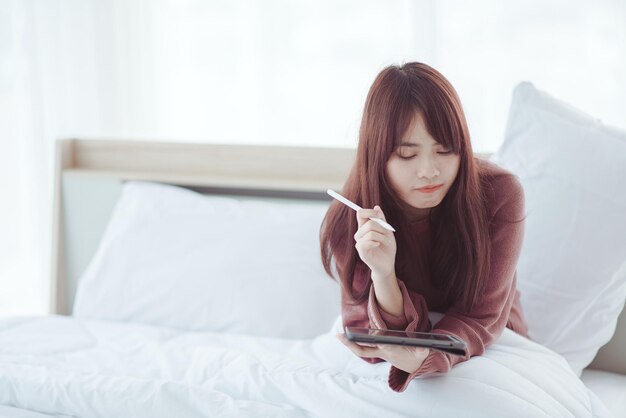 Eine Frau spielt ein Tablet auf dem Bett in einem weißen Schlafzimmer