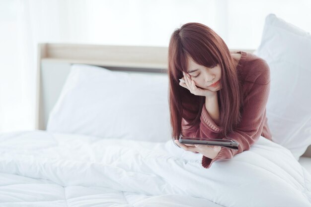 Eine Frau spielt ein Tablet auf dem Bett in einem weißen Schlafzimmer