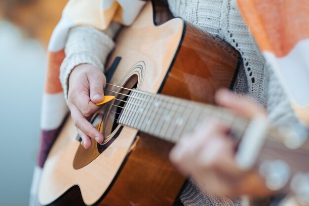 Eine Frau spielt Gitarre mit Hilfe eines Vermittlers in der Nähe des Wassers in der Natur und übt das Spielen des Instruments an einer kühlen Herbstabendzeit an der frischen Luft.