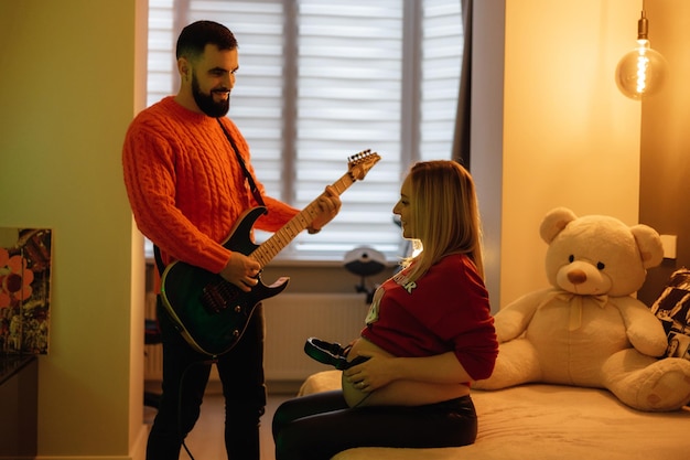 Eine Frau spielt mit einem Mann in einem roten Pullover Gitarre.