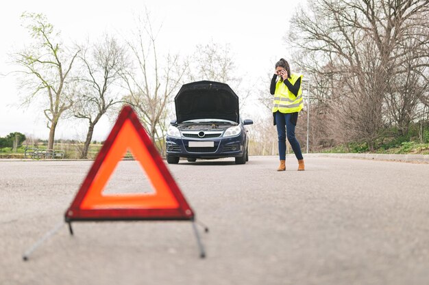 Eine Frau spricht mit ihrem Handy, während ihr Auto auf der Straße kaputt ist