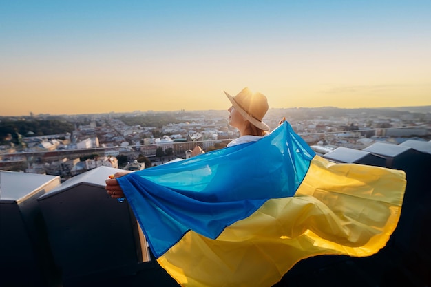 Eine Frau steht mit der ukrainischen Nationalflagge und schwenkt sie und betet für den Frieden bei Sonnenuntergang in LvivxAA Symbol der Unabhängigkeit und Stärke des ukrainischen Volkes. Beten Sie für die Ukraine