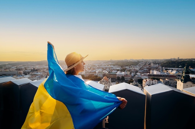 Eine Frau steht mit der ukrainischen Nationalflagge und schwenkt sie und betet für den Frieden bei Sonnenuntergang in LvivxAA Symbol der Unabhängigkeit und Stärke des ukrainischen Volkes. Beten Sie für die Ukraine