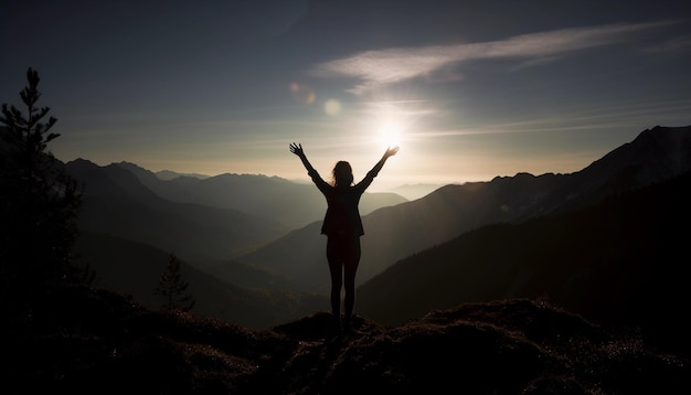 Eine Frau steht mit erhobenen Armen auf einem Berggipfel, hinter ihr scheint die Sonne.