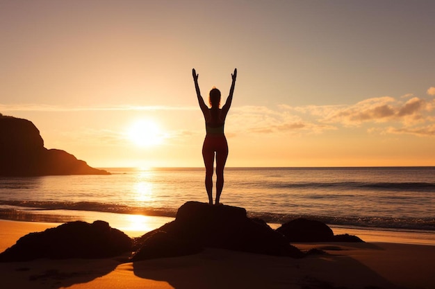 Eine Frau steht mit erhobenen Armen auf einem Felsen, während die Sonne über dem Meer untergeht.