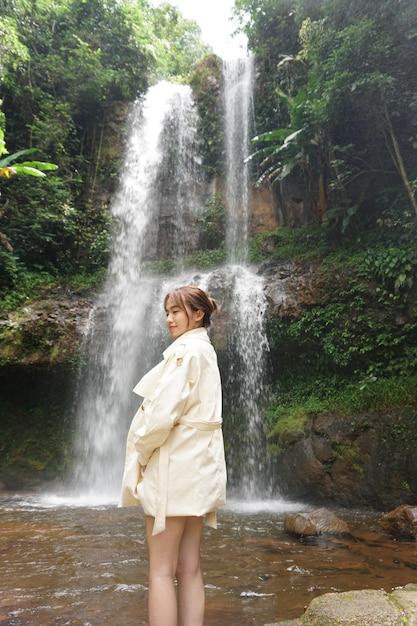 Eine Frau steht vor einem Wasserfall im Dschungel.