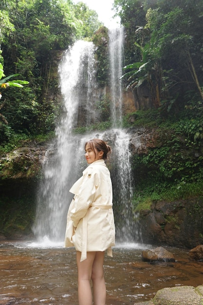Eine Frau steht vor einem Wasserfall im Dschungel.