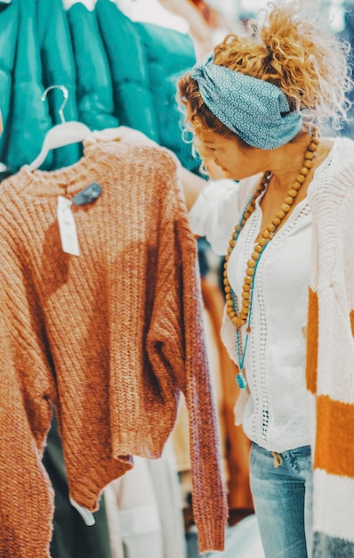 Foto eine frau sucht kleidung in einem laden weibliche menschen und mode-stil geschäftsjob oder einkaufsaktivität trendige dame sucht pullover in einem geschäft während der rabatt-ferienzeit