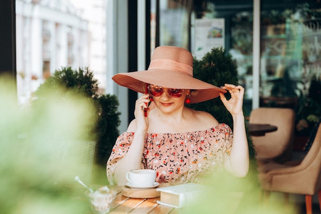 Eine Frau telefoniert Eine Frau mit einem Mobiltelefon sitzt in einem Café Eine Frau in einem Kleid und einem Hut in einem Café