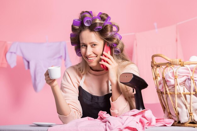 Eine Frau telefoniert mit einer Freundin und klatscht, während sie in einer Pause von der Hausarbeit Kaffee trinkt