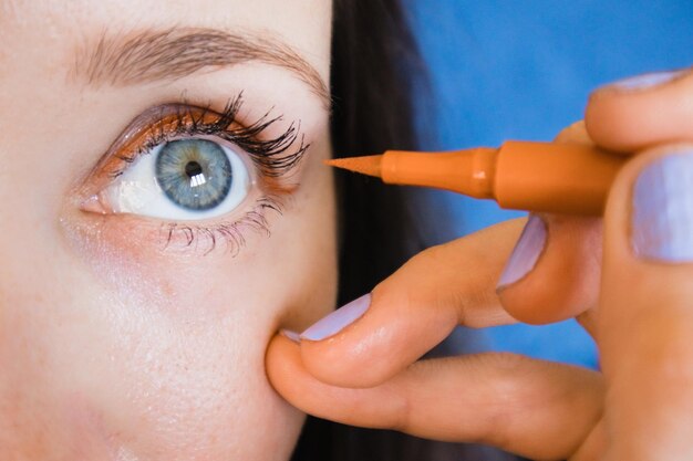 Foto eine frau trägt eyeliner auf ihr auge auf. frauenporträt vor blauer wand. blauäugige frau