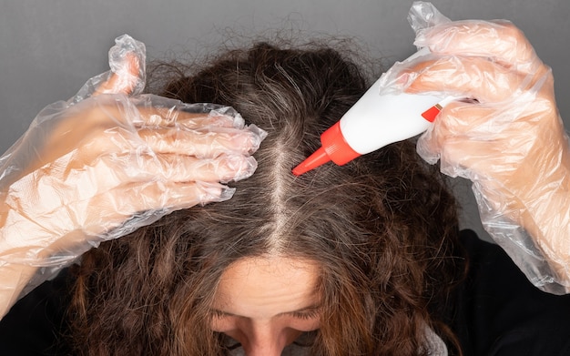 Eine Frau trägt Farbe auf die Wurzeln ihrer Haarfarben auf grauem Haar auf