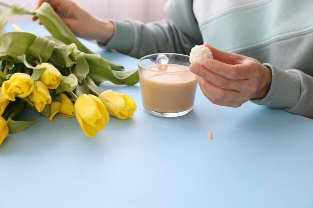 Eine Frau trinkt Kaffee mit Süßigkeiten und einem Strauß gelber Tulpen auf dem Tisch