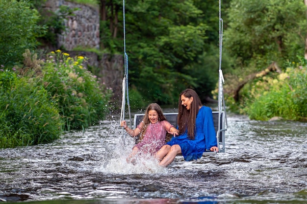 Eine Frau und ein junges Mädchen schwingen sich lachend und plätschernd über einen schnell fließenden Fluss