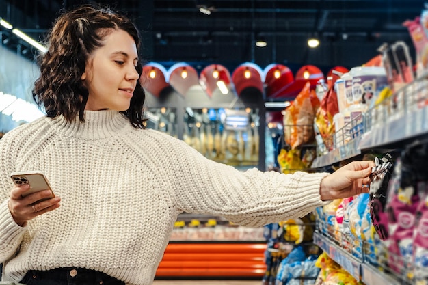 Eine Frau wählt in einem Supermarkt am Telefon ein Produkt aus einer Produktliste aus