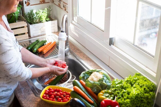 Eine Frau wäscht die Ernte in der Küche Kleine Tomaten unter einem Wasserstrahl und viel Gemüse