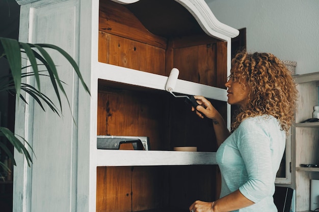 Eine Frau zu Hause, die allein ein altes Holzschrankmöbel mit weißem Pinsel renoviert Empowerment Heimwerker-Konzept Lifestyle-Arbeit im Innenbereich Freizeitaktivität mit Vintage-Restaurierungshobby im Inneren