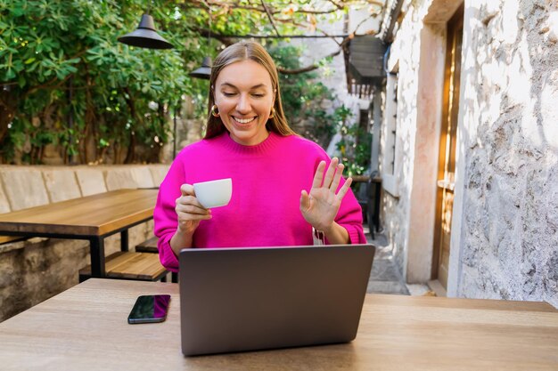 Eine Freiberuflerin während eines Anrufs mit einem Team, das in einem Café sitzt Der Laptop steht auf dem Tisch Fernarbeit