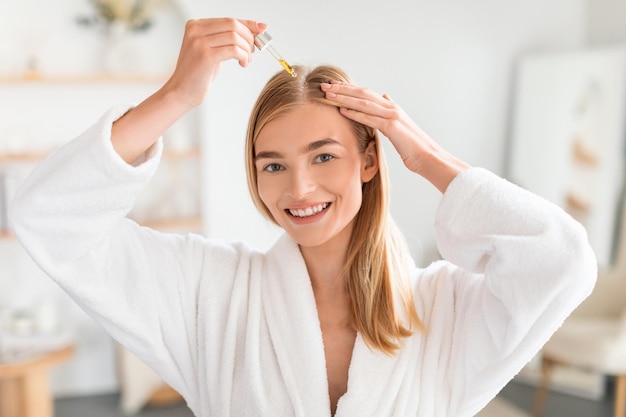 Foto eine freudige frau behandelt die haarwurzeln, indem sie im badezimmer ein nahrhaftes serum aufträgt