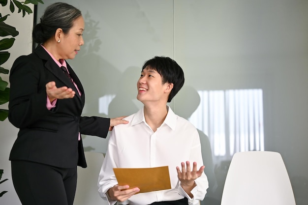 Eine freundliche ältere asiatische Geschäftsfrau versucht, einen Kandidaten zu trösten, indem sie vor einem Vorstellungsgespräch spricht