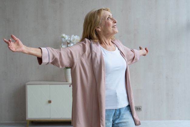 Eine fröhliche ältere Frau hört Musik und tanzt in ihrem Wohnzimmer