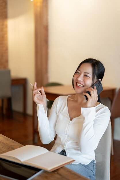 Eine fröhliche asiatische Frau genießt es, mit ihrer Freundin zu telefonieren, während sie in einem Café entspannt