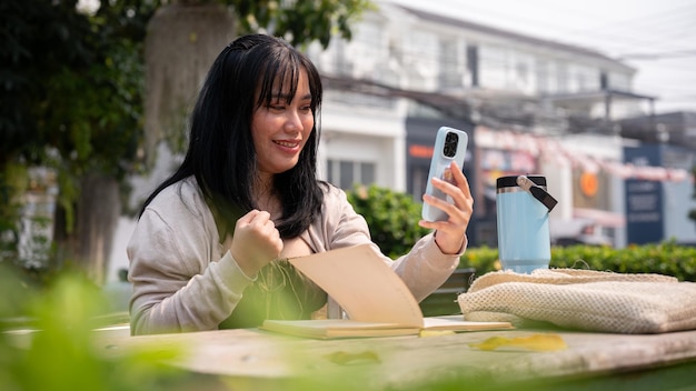 Eine fröhliche asiatische Frau schaut mit einem äußerst glücklichen Gesicht auf den Bildschirm ihres Smartphones