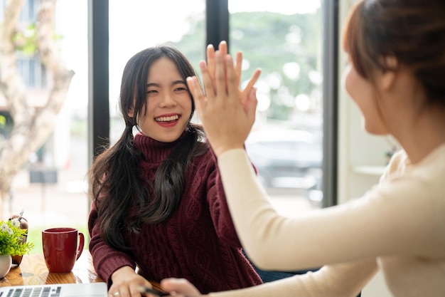 Eine fröhliche junge asiatische Frau gibt ihrer Freundin ein High Five, um sie aufzuheitern