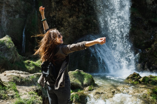 Eine fröhliche junge Frau, die den Blick auf den wunderschönen Wasserfall genießt.