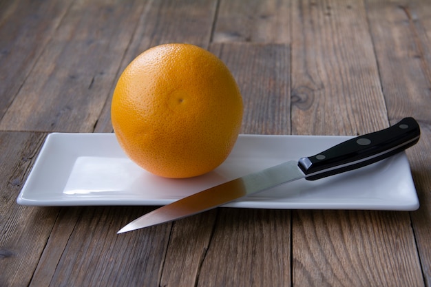 eine ganze Grapefruit auf einem weißen Teller mit einem schwarzen Messer