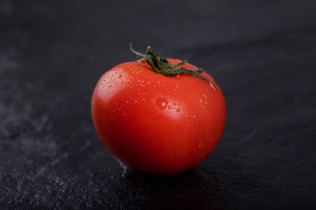 Eine ganze rote frische Tomate platziert auf einem schwarzen Hintergrund.