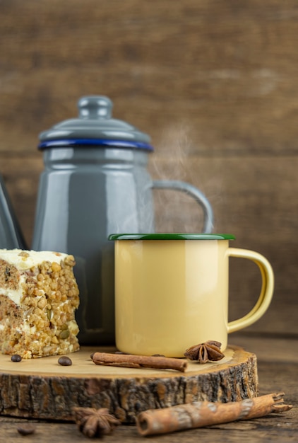 Eine gelbe Zinn-Tasse heißen Tees mit Teekanne und Kuchen auf Holztisch.