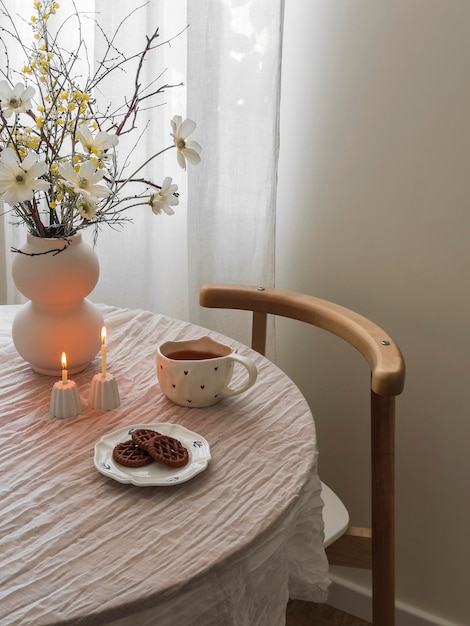 Eine gemütliche Kaffeepause, eine Tasse Kaffeekekse, zündende dünne Kerzen in Kerzenstöcken, eine Vase mit Blumen auf einem runden Tisch im Wohnzimmer