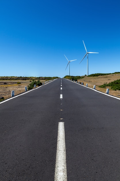 Eine gerade Straße mit zwei Windkraftanlagen über dem Gebiet mit einem blauen Himmel