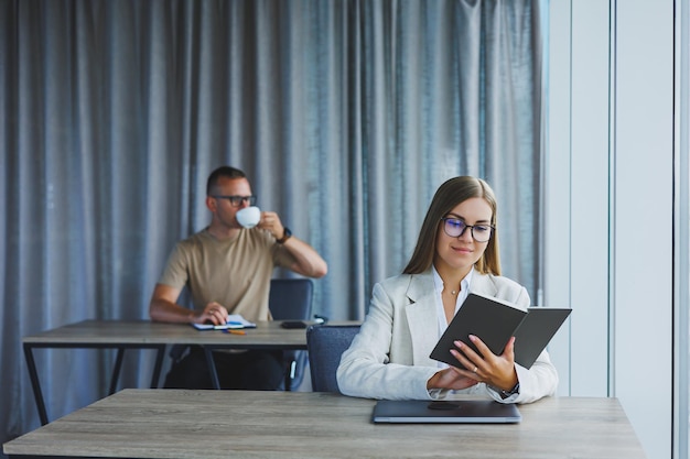 Eine Geschäftsfrau hält einen Notizblock und benutzt einen Laptop, während ihr europäischer Kollege im Hintergrund arbeitet Konzept moderner erfolgreicher Frauen Büroangestellte, die an Schreibtischen im Büro sitzen