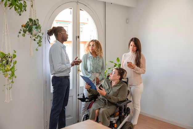 Eine Geschäftsfrau im Rollstuhl mit einer Behinderung bespricht mit ihren gemischtrassigen Kollegen in der Nähe des Fensters die Geschäftsstrategie